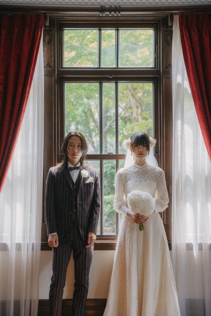 洋館の窓辺に立つ新郎新婦